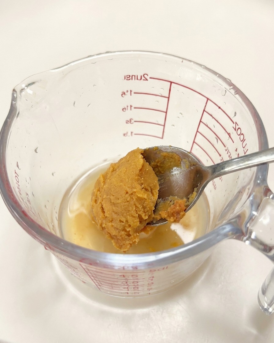 Łyżka pasty miso dodawana do naczynia z płynnymi przyprawami.