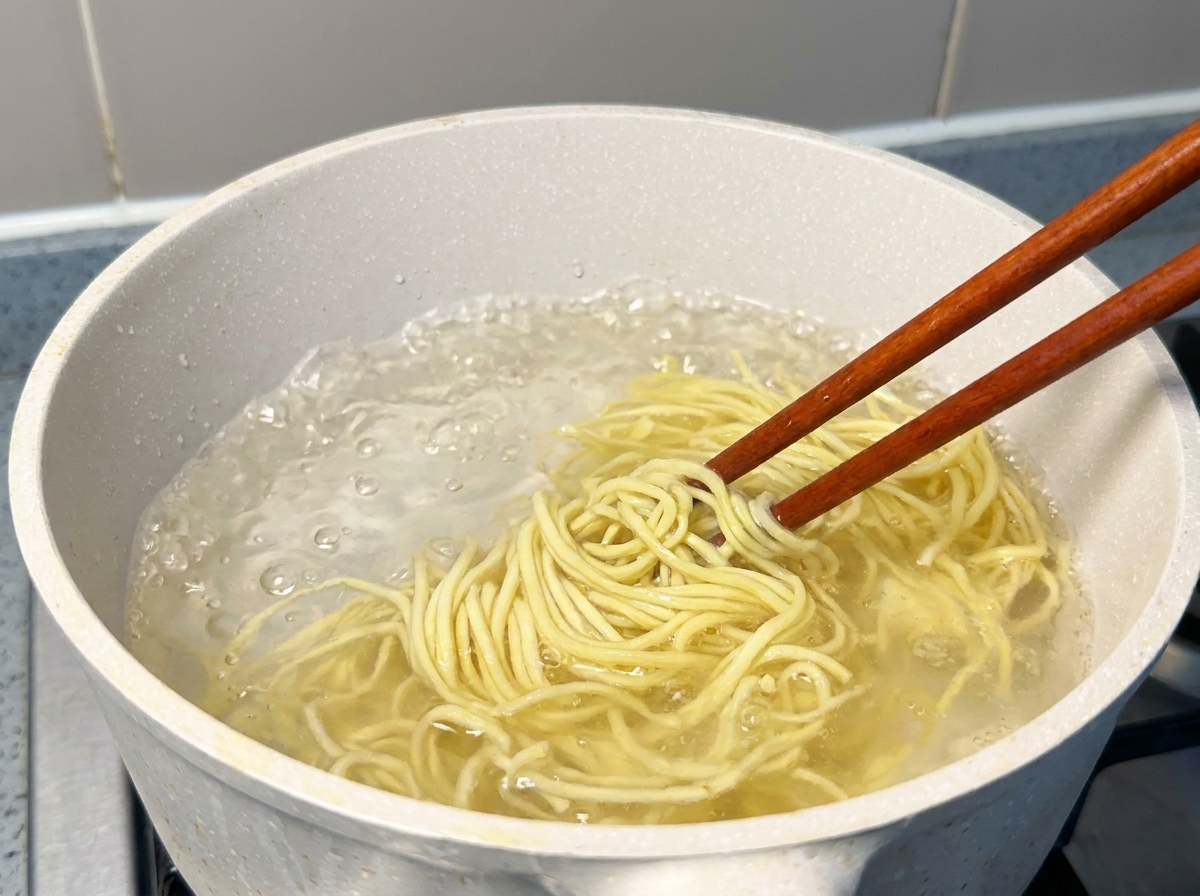 Świeży żółty makaron ramen unoszony pałeczkami z garnka z wrzącą wodą.