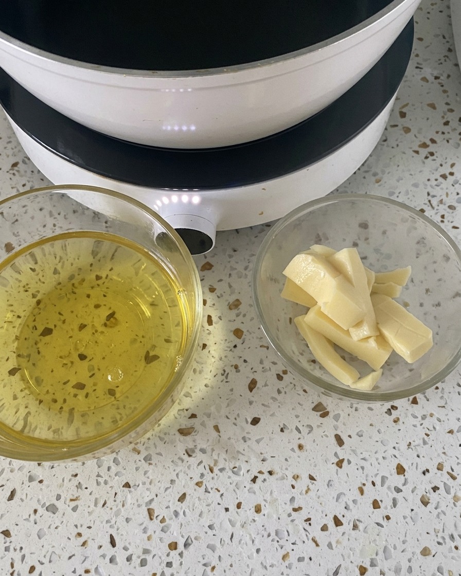 Dwie małe szklane miseczki z wbitymi jajkami i plastrami sera mozzarella, stojące na białym blacie obok kuchenki.