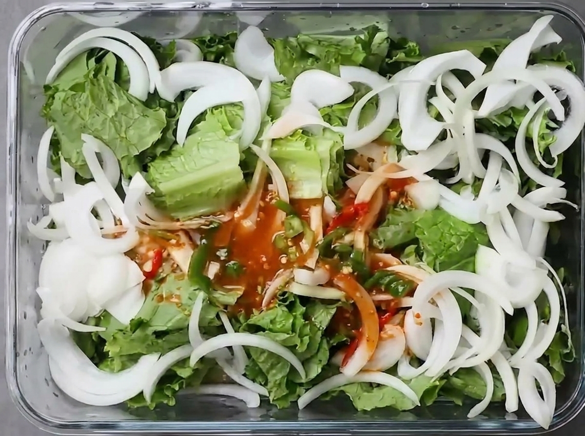 Czerwony bulion chili z posiekanym zielonym chili wylewany na świeżą, porwaną sałatę i pokrojoną w plastry białą cebulę w prostokątnym pojemniku na żywność.