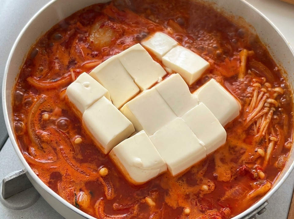 Duże kostki miękkiego białego tofu w gorącym, bulgoczącym koreańskim gulaszu kimchi.