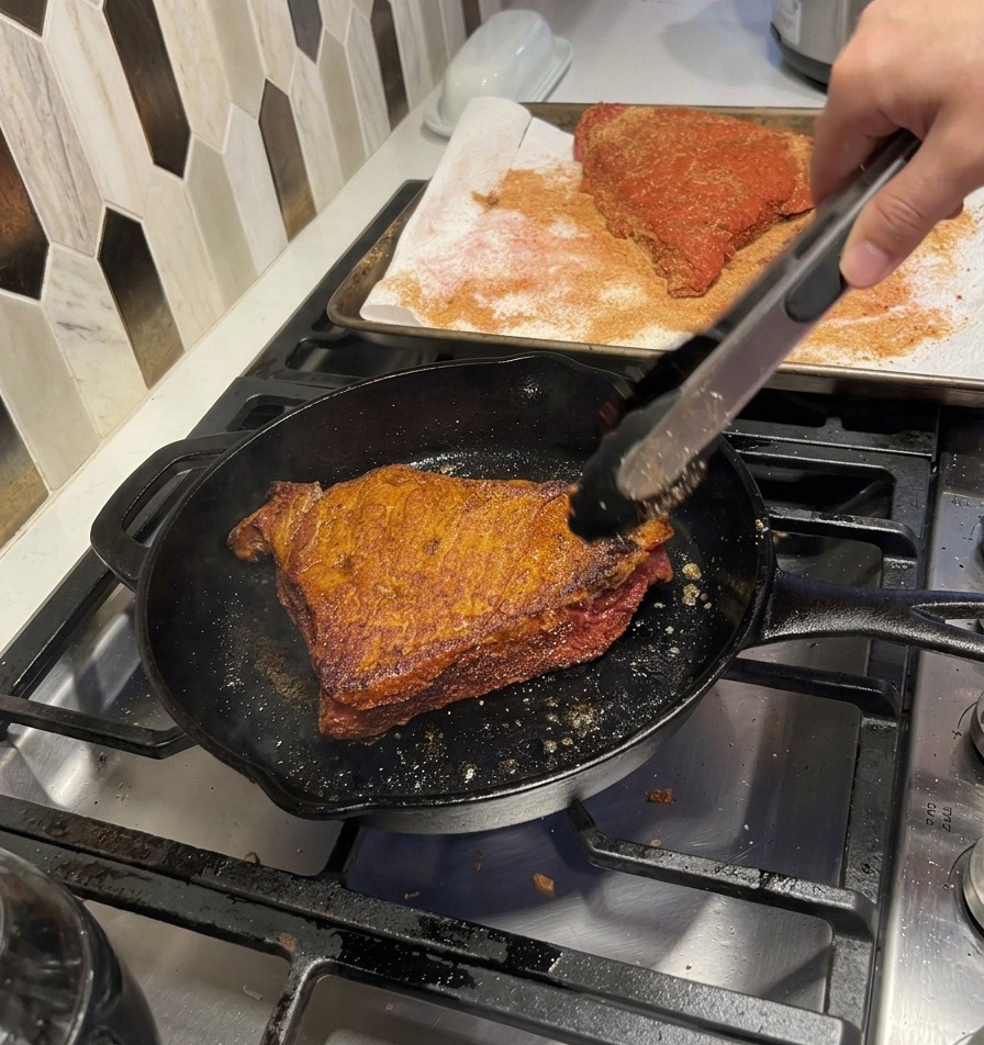 Kilka kawałków doprawionej wołowiny równomiernie brązujących się na gorącej żeliwnej patelni.