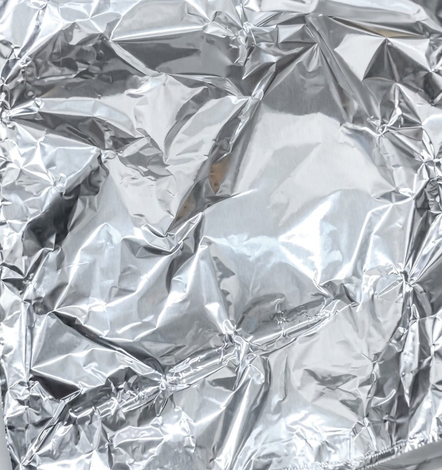 Zbliżenie na składanie i uszczelnianie brzegów folii aluminiowej wokół marynowanego mięsa.