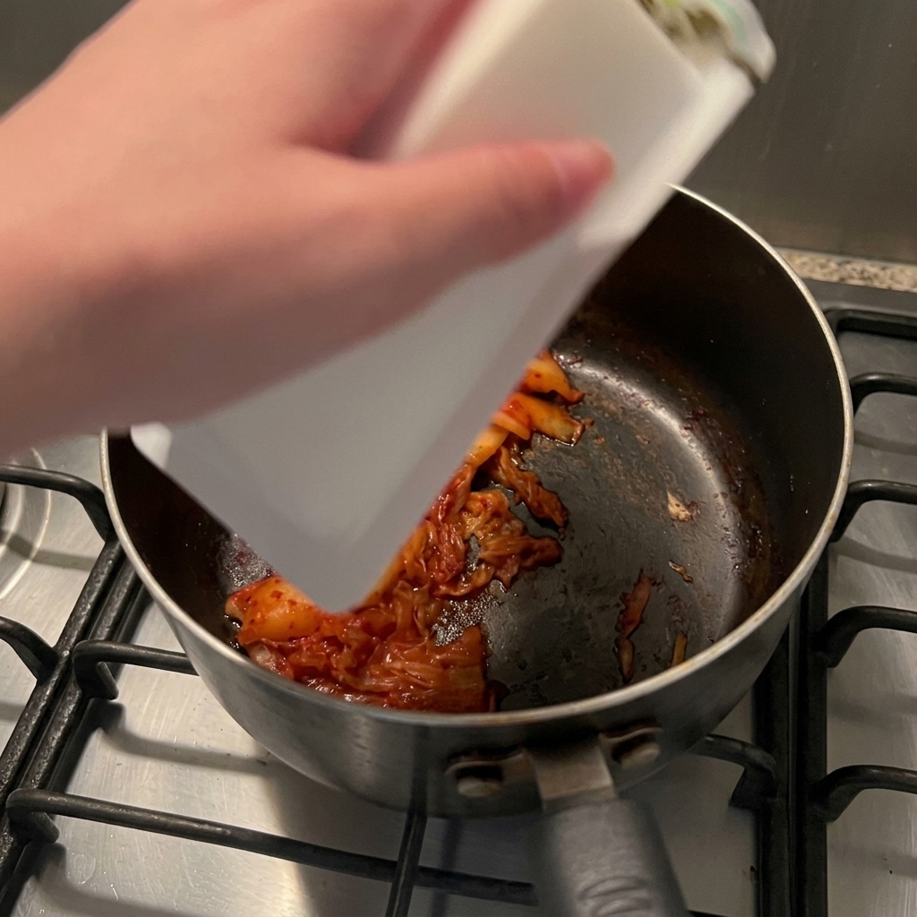 Blok białego tofu jedwabistego wysuwający się z plastikowego opakowania do rondla z podsmażonym kimchi.