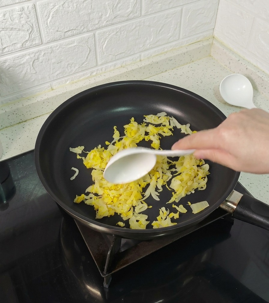 Łopatka mieszająca żółtą kapustę kiszoną na czarnej patelni teflonowej.