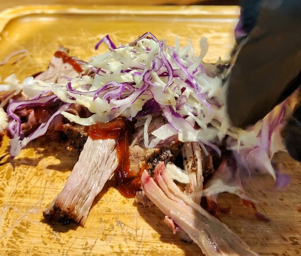 Nakładanie poszatkowanej białej i czerwonej kapusty bezpośrednio na wieprzowinę w sosie BBQ na desce.