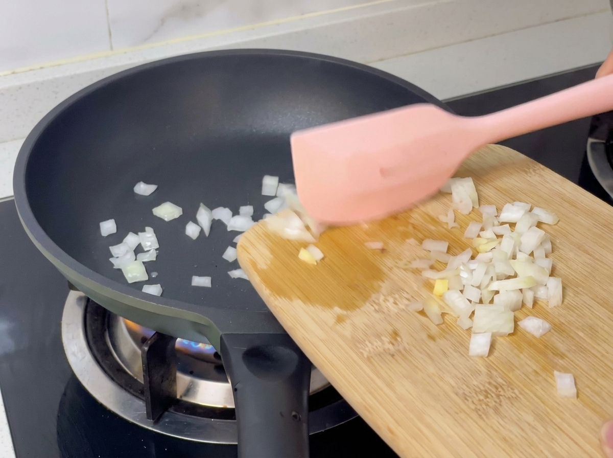 Cebula przekładana z deski na gorącą patelnię za pomocą różowej łopatki.