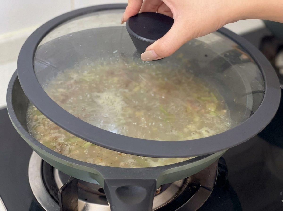 Ręka kładąca szklaną pokrywkę na patelnię z gotującą się bazą do chowdera.