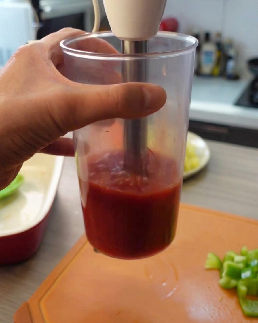 Użycie blendera ręcznego do zmiksowania pomidorów z puszki w wysokim, przezroczystym pojemniku na gładkie purée.