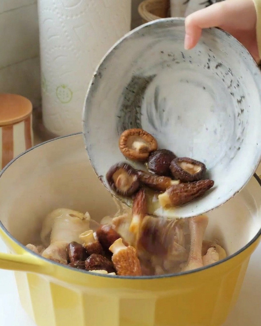 Miska namoczonych grzybów shiitake i smardzów wlewana do garnka z kurczakiem.
