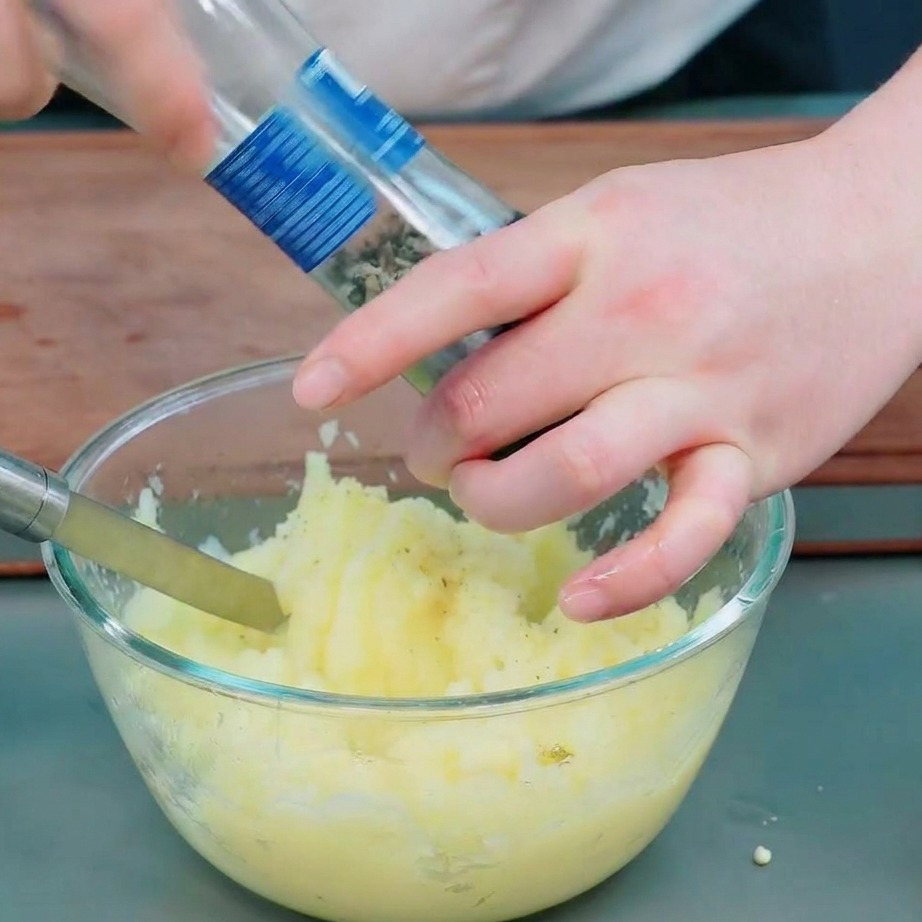 Dłonie dodają świeżo mielony pieprz i sól do gładkiego purée ziemniaczanego w misce.