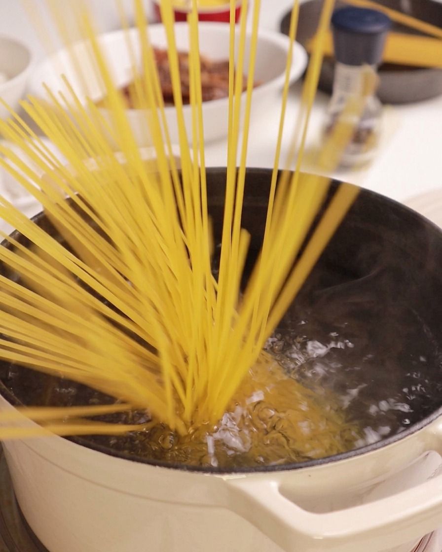 Pęczek suchego makaronu spaghetti wrzucany do garnka z wrzącą wodą.