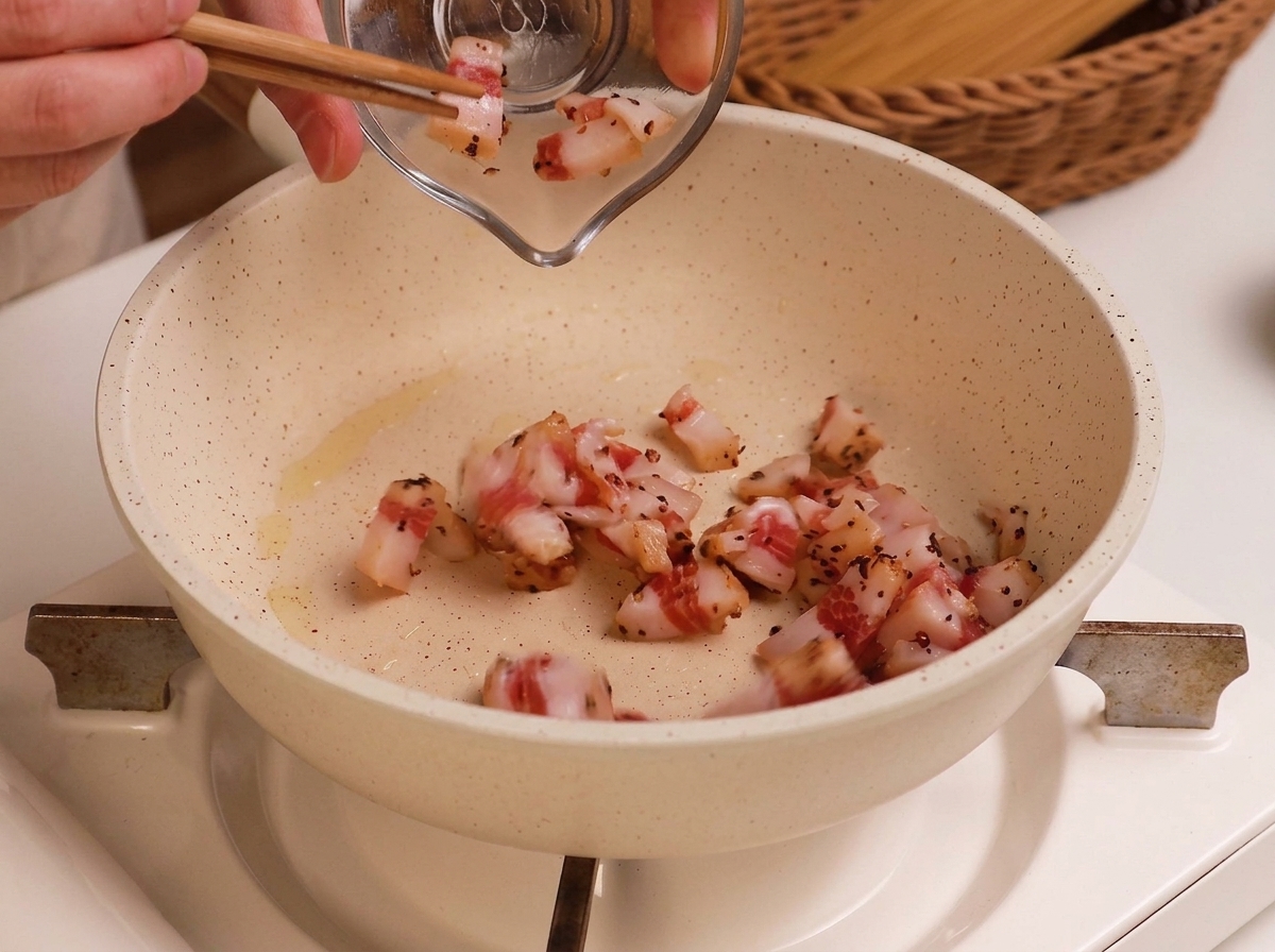 Pokrojone w kostkę surowe guanciale przekładane z małej szklanej miseczki na lekko natłuszczoną białą patelnię.