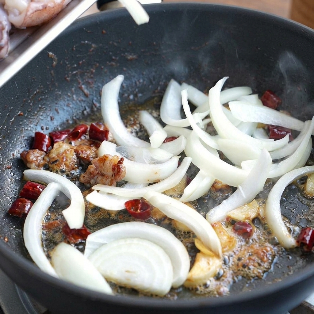 Pokrojona biała cebula mieszana na patelni z aromatyzowanym olejem, suszonym chili i czosnkiem.
