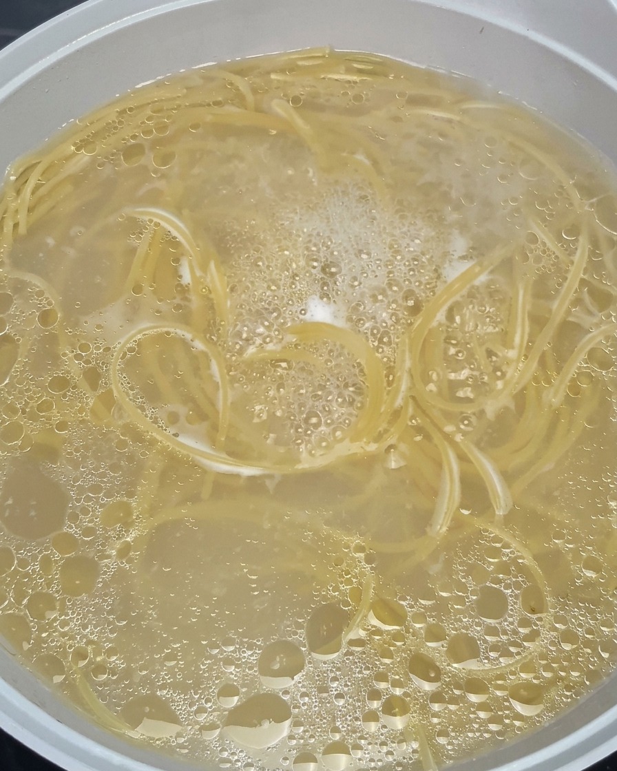 Makaron spaghetti mięknący i wirujący w garnku z mocno wrzącą, bąbelkową wodą.