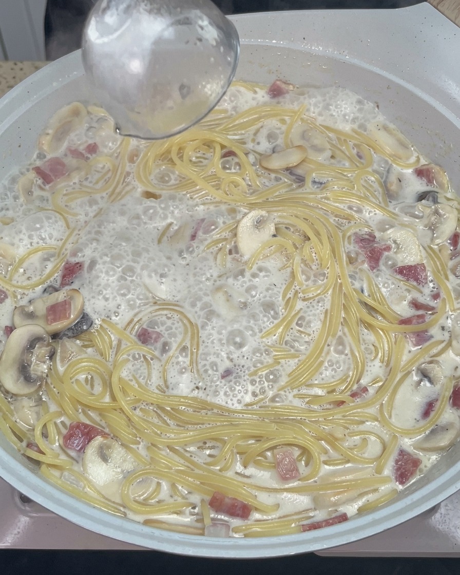 Drewniana łyżka mieszająca kremowe spaghetti z roztopionym serem i przyprawami na ciepłej patelni.