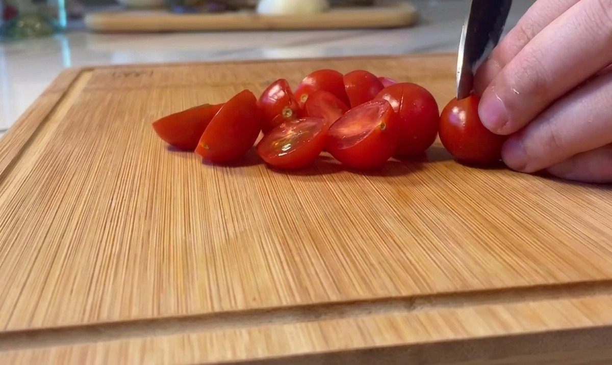 Przecinanie jaskrawoczerwonych pomidorków koktajlowych na pół na drewnianej desce.