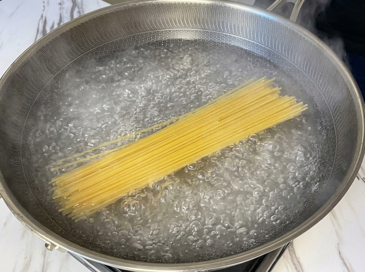 Suchy makaron spaghetti zanurzony w szerokim garnku z intensywnie wrzącą wodą.