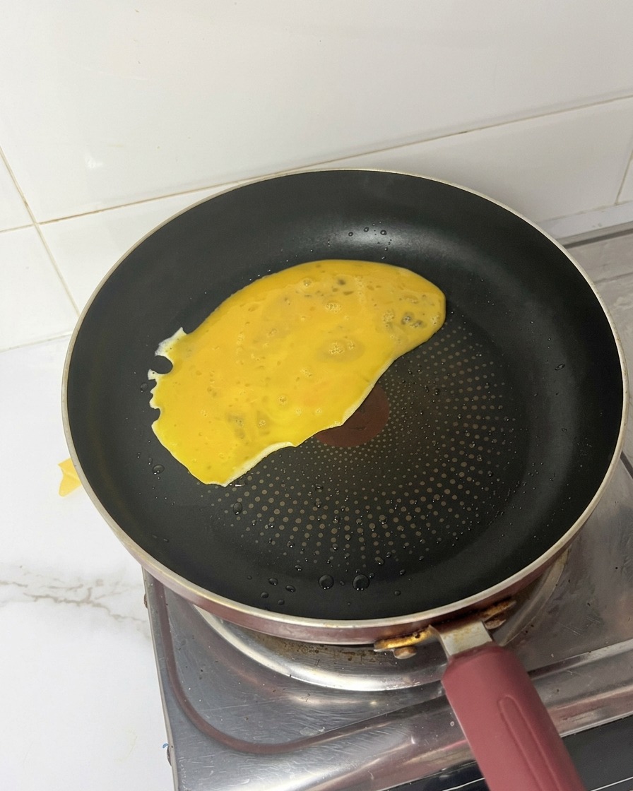 Żółta masa jajeczna wlewana na gorącą czarną patelnię.