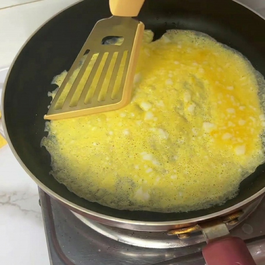 Cienki żółty omlet dzielony na cztery części metalową łopatką na patelni.