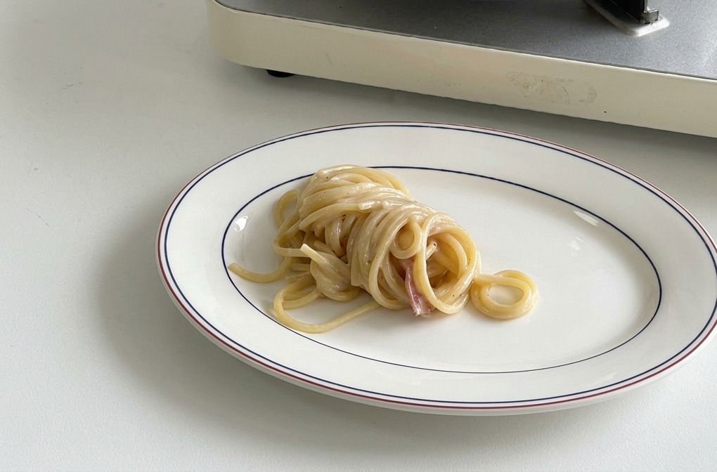Starannie zwinięta porcja spaghetti na środku białego talerza z niebiesko-czerwonym rantem.