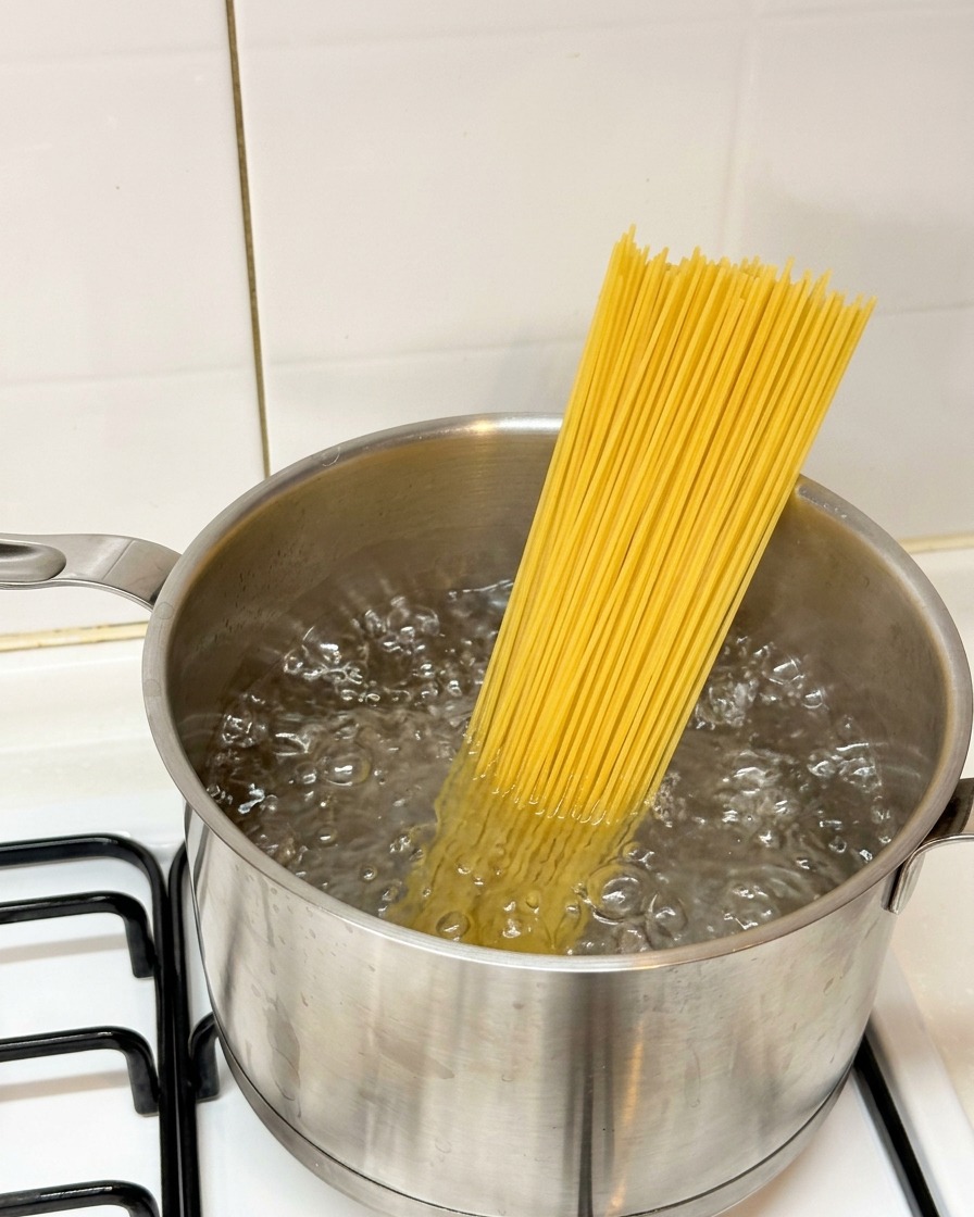 Surowy makaron spaghetti wkładany do garnka z wrzącą wodą.