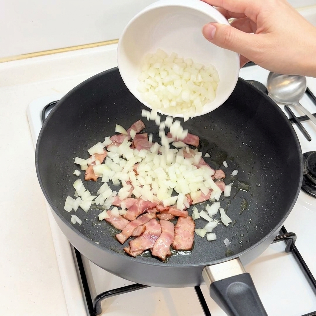 Wsypywanie posiekanej cebuli z białej miseczki na patelnię z boczkiem.