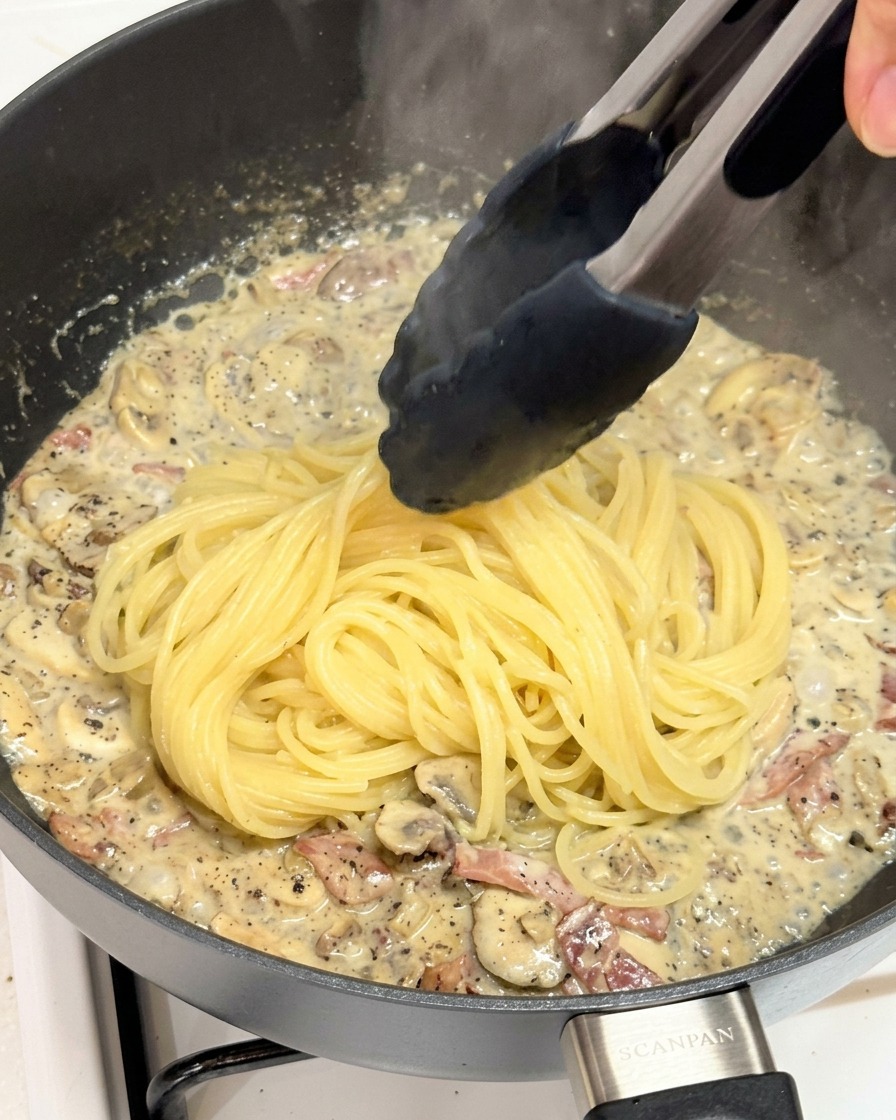 Przekładanie ugotowanego spaghetti szczypcami do patelni z sosem truflowym.