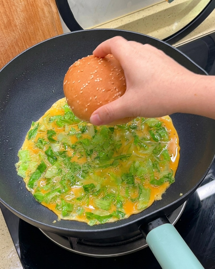 Ręka kładąca połówkę bułki do burgera stroną rozciętą do dołu na smażący się omlet.