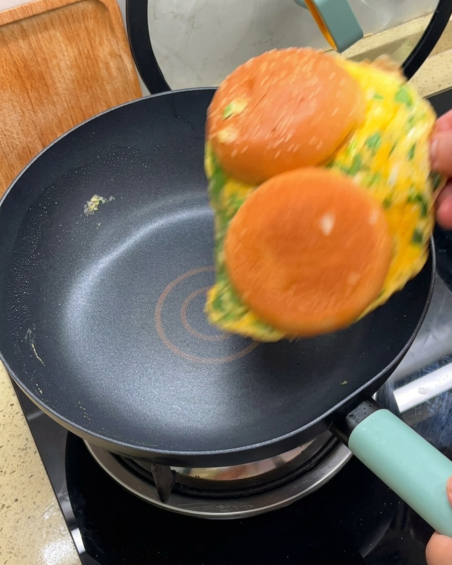 Omlet z dwiema przyklejonymi połówkami bułek obracany na patelni za pomocą łopatki.