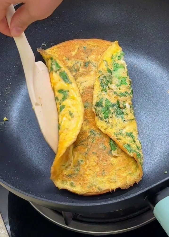 Łopatka zawijająca brzegi zielonego omletu na podpieczone połówki bułek na patelni.