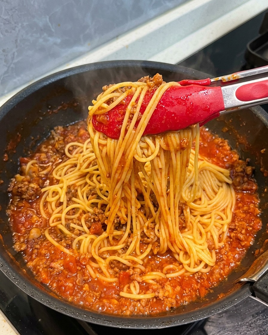 Czerwone szczypce unoszące pęczek spaghetti dokładnie oblepionego bogatym sosem pomidorowo-mięsnym.