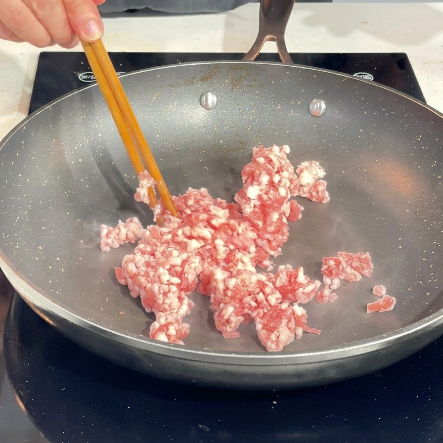 Rozdzielanie surowego mięsa mielonego za pomocą pałeczek na gorącej patelni.