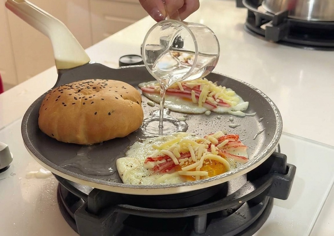 Wlewanie czystej wody z małej szklanki na gorącą patelnię między bułkę a jajka.