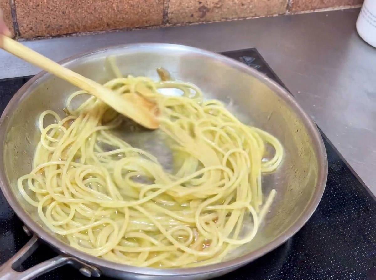 Spaghetti mieszane na patelni drewnianą łyżką, aby każda nitka pokryła się sosem.