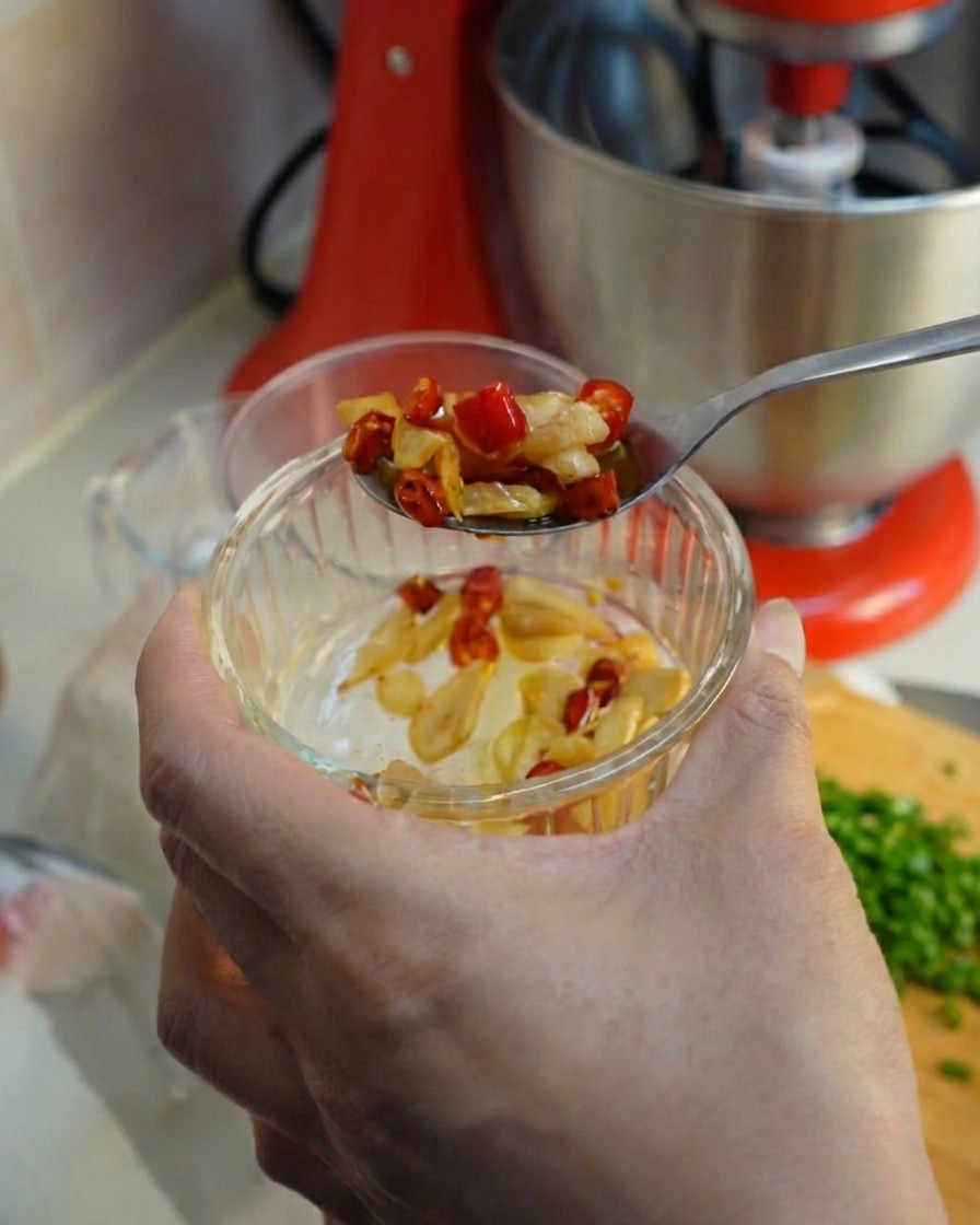 Łyżka nabierająca smażony czosnek i chili z małej szklanej miseczki.