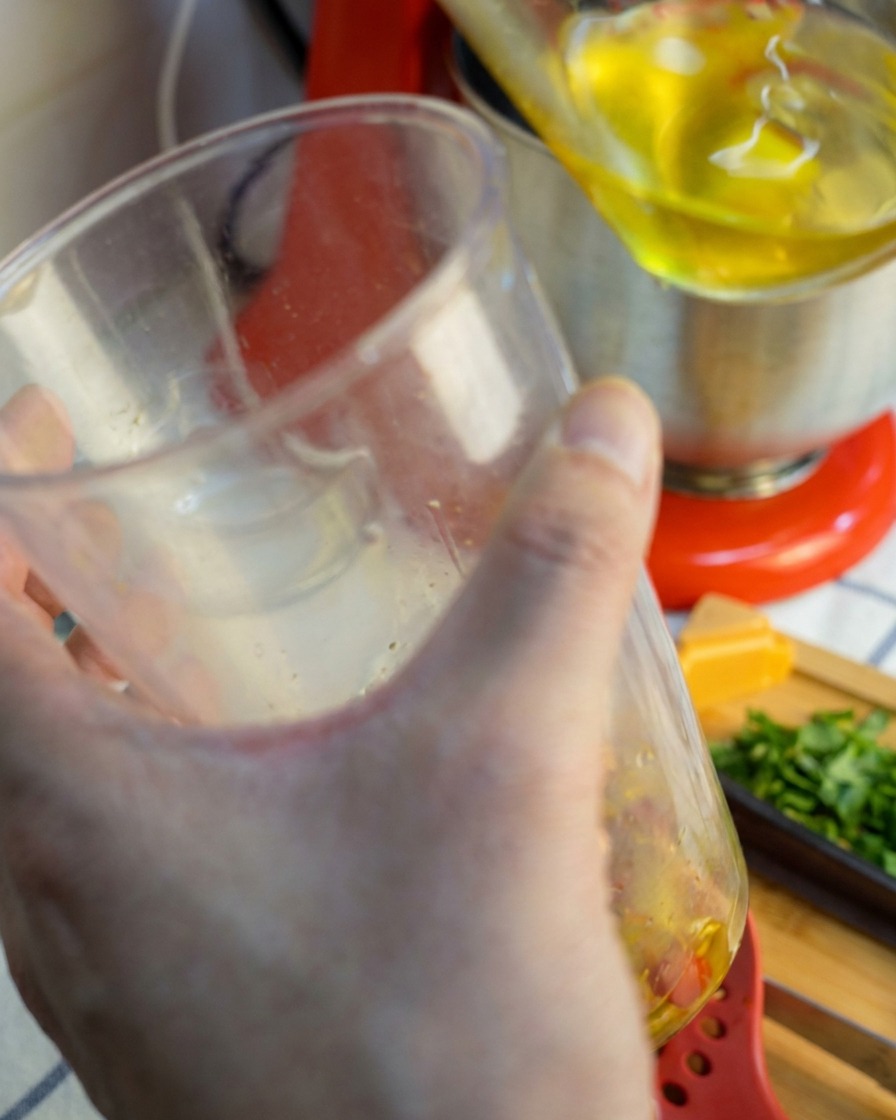 Blender ręczny wyjmowany z przezroczystego pojemnika, z którego ścieka gładki, złocisto-czerwony sos czosnkowo-chili.