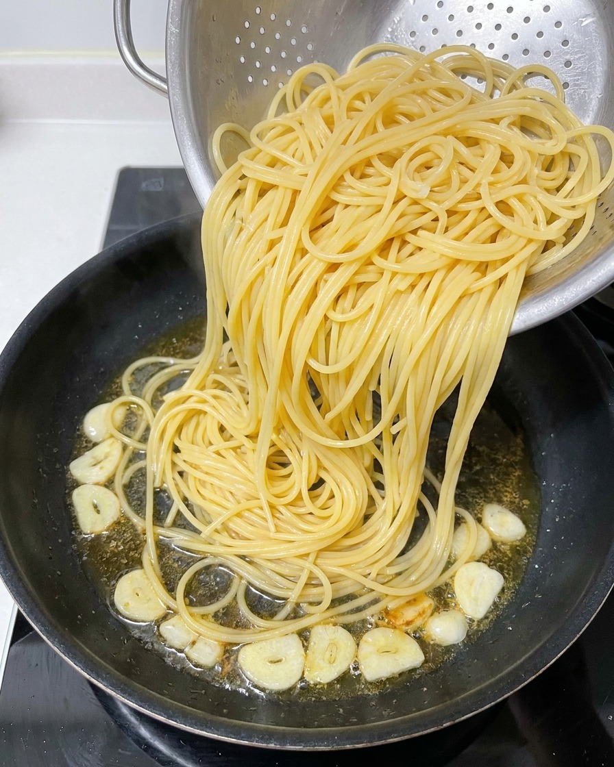 Ugotowane spaghetti przekładane z metalowego cedzaka na patelnię z resztką aromatycznej oliwy.