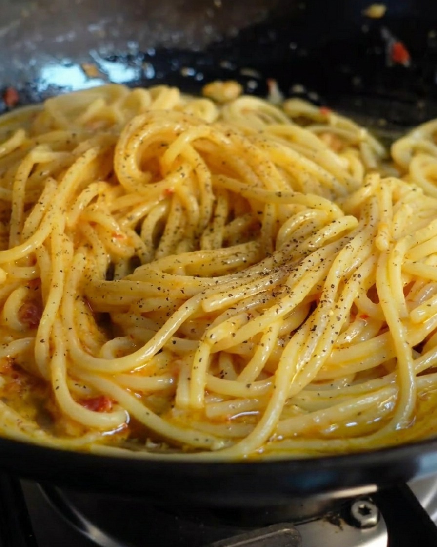 Świeżo zmielony czarny pieprz posypany na błyszczące spaghetti na patelni.