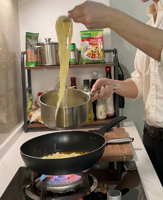 Długie nitki ugotowanego makaronu spaghetti wyciągane z garnka szczypcami na gorącą patelnię z przyprawioną oliwą.