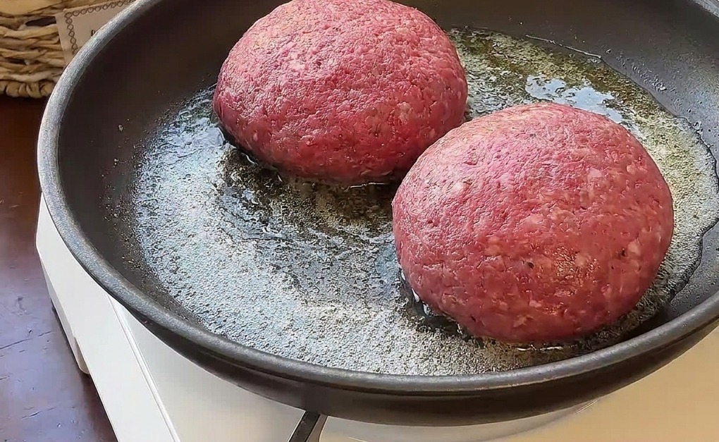 Dwa grube kotlety wołowe smażone na roztopionym maśle na patelni.