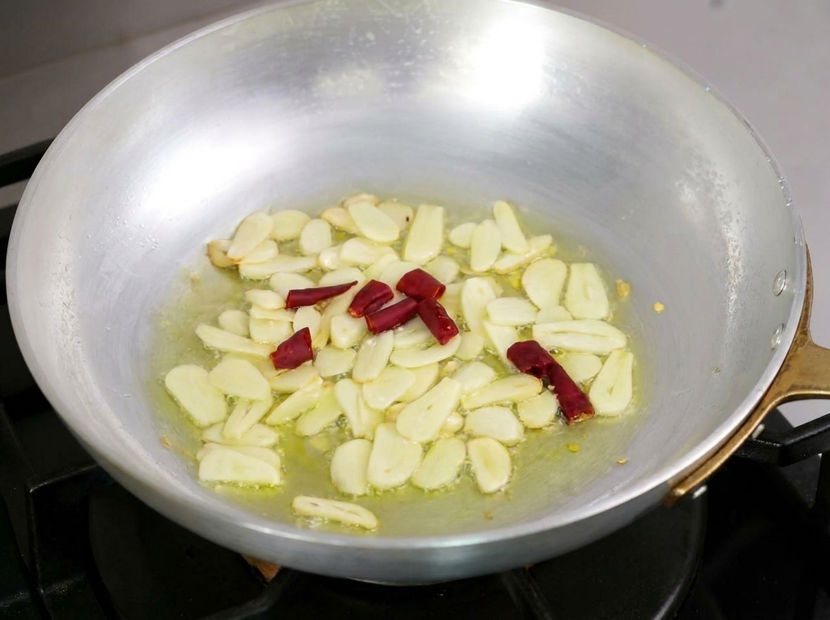 Plasterki czosnku i kawałki suszonego chili delikatnie smażące się w oliwie na patelni.