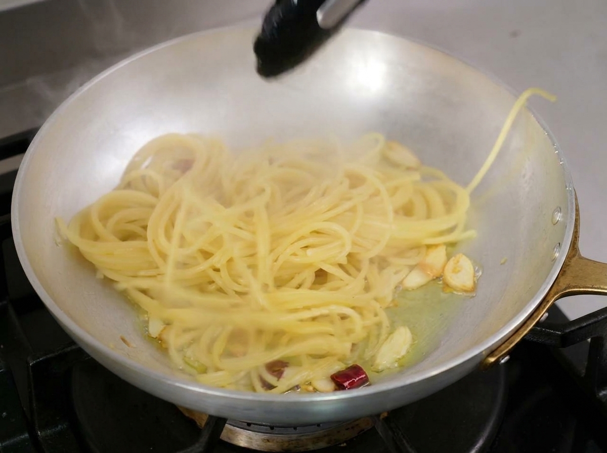Ugotowane spaghetti przekładane szczypcami prosto do patelni z oliwą czosnkową i chili.