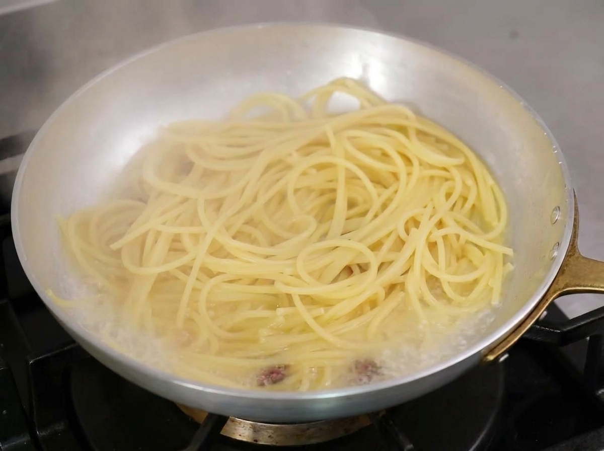 Spaghetti gotujące się na patelni z bąbelkującą, mętną wodą z makaronu i oliwą.