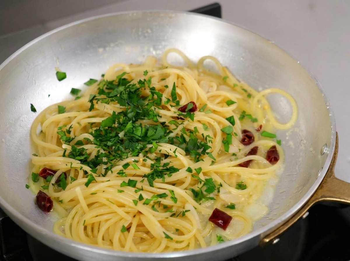 Posiekana świeża natka pietruszki obficie posypana na ugotowane spaghetti na patelni.