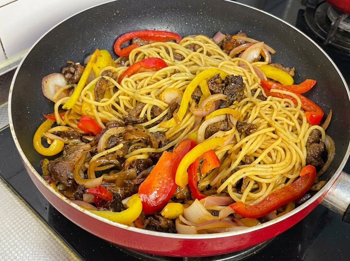 Spaghetti z czarnym pieprzem, wołowiną i kolorową papryką dokładnie wymieszane i lśniące od sosu na patelni.