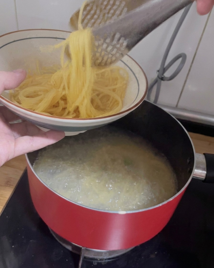 Szczypce wyjmujące ugotowane spaghetti z garnka do wzorzystej ceramicznej miski.