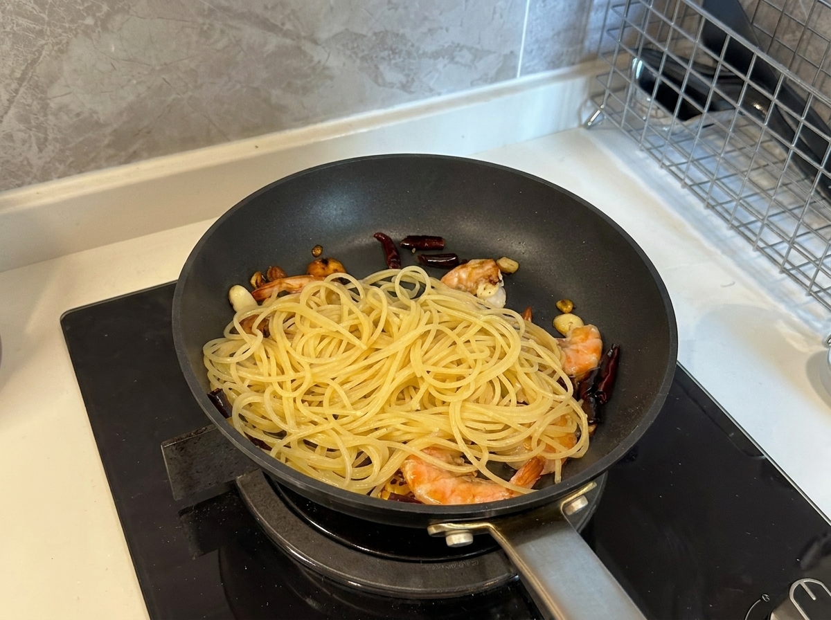 Ugotowany makaron spaghetti dodawany na patelnię pełną krewetek, czosnku i chili.
