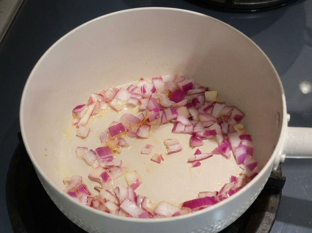 Posiekana czerwona cebula smażąca się na oleju na jasnej patelni.