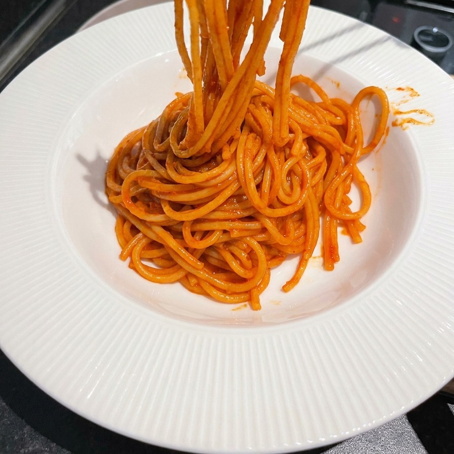 Metalowe pałeczki nabierające i zwijające jaskrawoczerwone, pokryte sosem spaghetti na biały talerz.